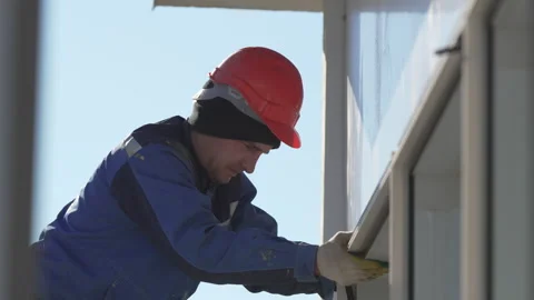 Builder in helmet installs window frame onto building facade Stock Footage 313829169