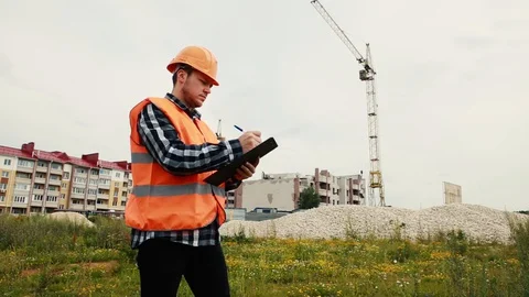 A builder in a helmet writes data against the background of a house under Stock Footage 129059919