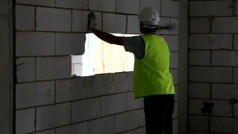 Builder in high vis with back to camera knocks down breeze block wall Stock Footage 112609380
