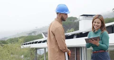 Builder holding board and manager tapping tablet on roof showing plan and Stock Footage 337886364