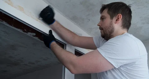 Builder with knife cuts mounting foam around perimeter of plastic window opening Stock Footage 129838429