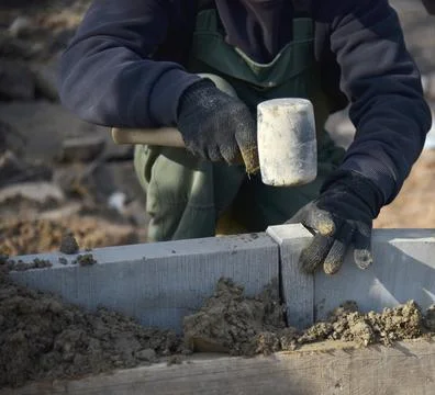 A builder knocks a hammer on a cement block, sets concrete curbs in the cement. 스톡 사진