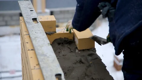 Builder lays bricks on the construction site during snowfall Stock Footage 103940492
