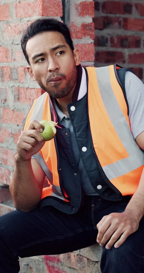 Builder, man and eating at construction site with break, fruit and thinking for Stock Footage 336265891