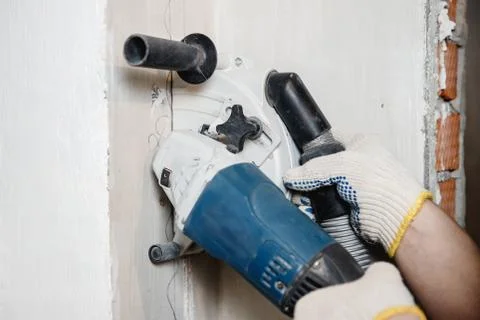Builder man cutting electrical chase in concrete wall with groove machine Stock Photos