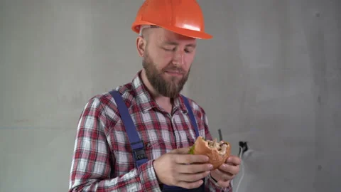 Builder man eating hamburger in a break on workplace Stock Footage 219924953