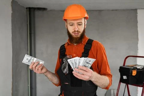 Builder man in hard hat and overalls counting money standing on constructio.. Stock Photos