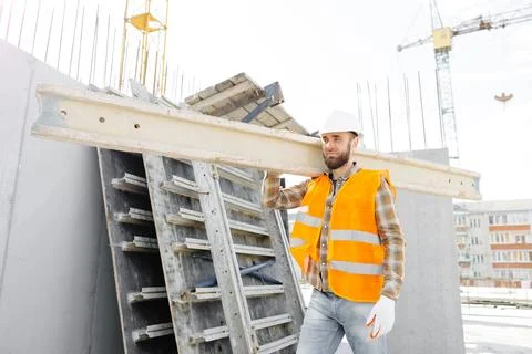 Builder man in hardhat and vest carrying timber on building site in his wor.. Stock Photos