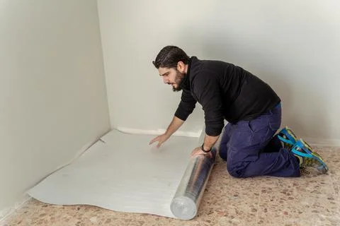 Builder man spreading the floor insulation to install the wooden floor Foto stock