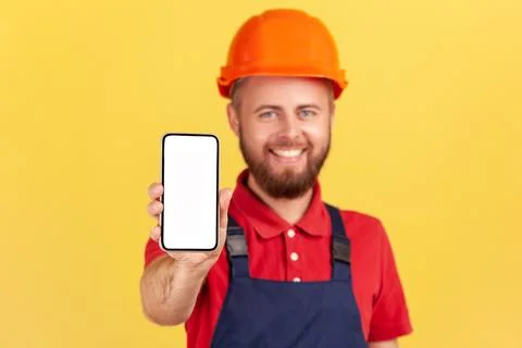 Builder man in uniform and protective helmet holding smart phone with blank Foto stock