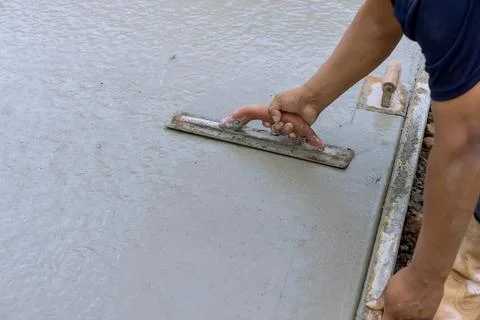 Builder mason worker leveling fresh concrete pavement wet cement using special Stock Photos