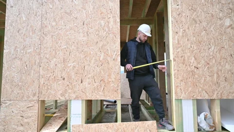 Builder measures doorway with tape measure inside unfinished wooden frame house Stock Footage 346541182