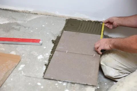 The builder measures the floor with a scoop to arrange the laying of ceramic til Stock Photos