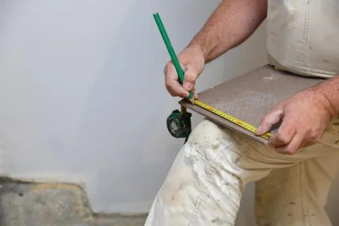 The builder measures the floor with a scoop to arrange the laying of ceramic til Stock Photos