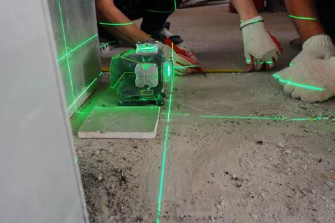 The builder measures the repair lines using a green laser level Stock Photos