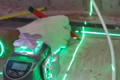 The builder measures the repair lines using a green laser level Stock Photos