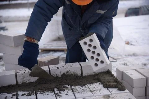 A builder in mittens puts gray bricks in cement in straight rows. Stock Photos