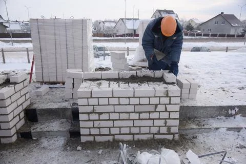 A builder in mittens puts gray bricks in cement in straight rows. Stock Photos