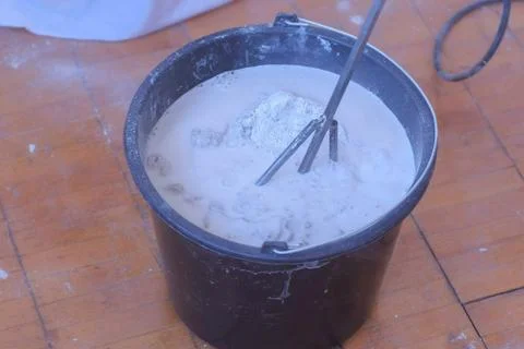Builder mixing cement plaster in bucket using an electric mixer, closeup view. Stock Photos