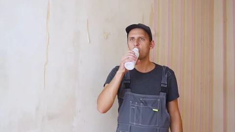 Builder or construction worker with pleasure drinks from a white bottle inside Видео 95216773