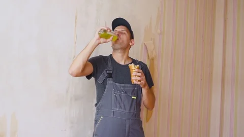Builder or construction worker with pleasure drinks from a bottle and eating a Видео 95217904
