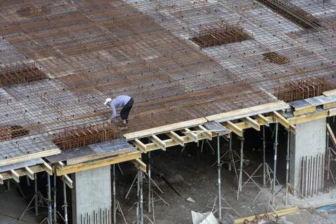 Builder in orange helmet works, construction of multi-storey building or Stock Photos