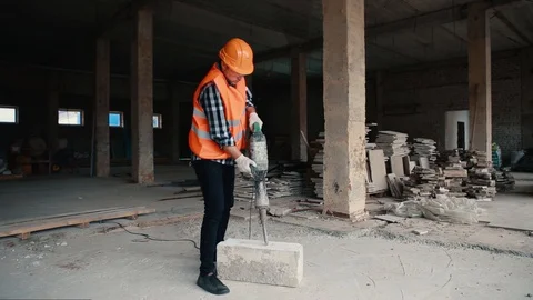 A builder in an orange vest and orange helmet works with a jackhammer. Stock Footage 129056277
