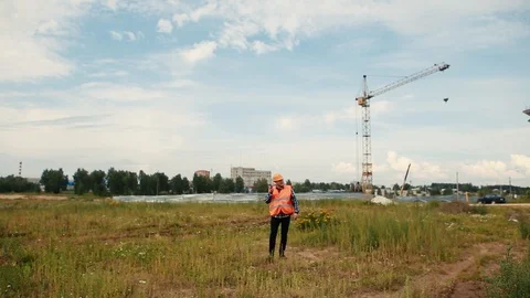 A builder in an orange vest and orange helmet walks on the walkie-talkie. Stock Footage 129056622