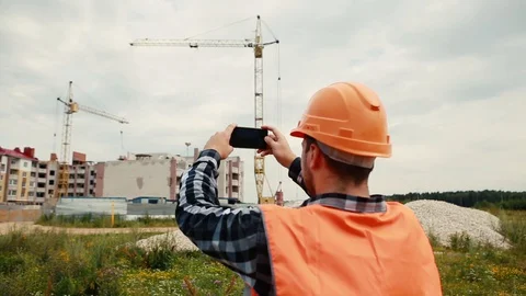 A builder in an orange vest and an orange helmet is filming a construction video Stock Footage 129056770