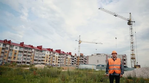 A builder in an orange vest and an orange helmet spreads his arms in different Stock Footage 129056836