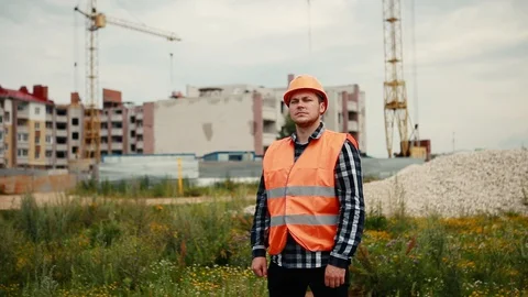 A builder in an orange vest and an orange helmet that stands against the Stock Footage 129057940