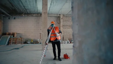 A builder in an orange vest and orange helmet is looking into a measuring device Stock Footage 129060205