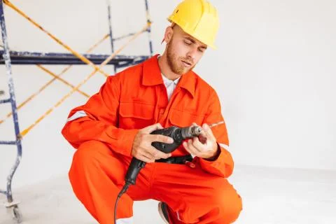 Builder in orange work clothes and hardhat thoughtfully using el Stock Photos