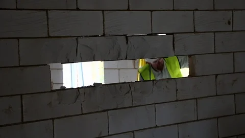 Builder on the other side of a wall after knocking out breeze blocks Stock Footage 112609305