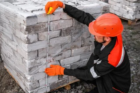 Builder packs bricks into pallets at construction site Stock Photos