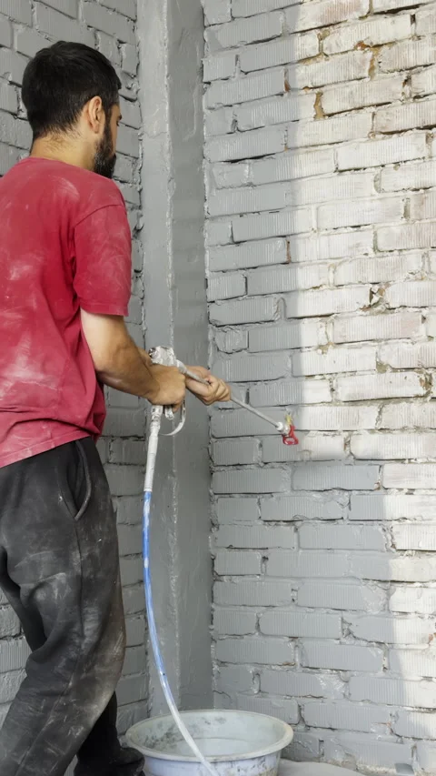 Builder paints brick wall in grey color with sprayer tool in building premise Stock Footage 323860929