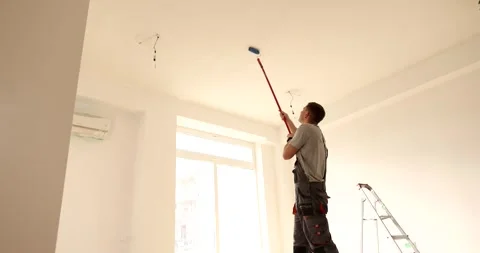 Builder paints ceiling with paint roller attached to handle Stock Footage 294194023