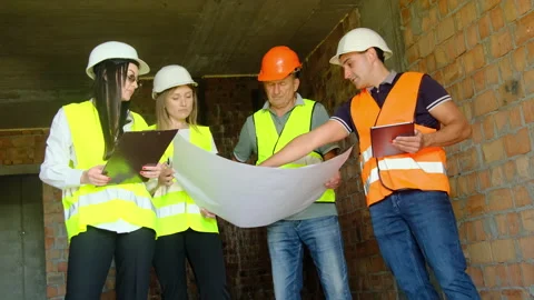 Builder points to fragment of floor plan standing near colleagues Stock Footage 317612253
