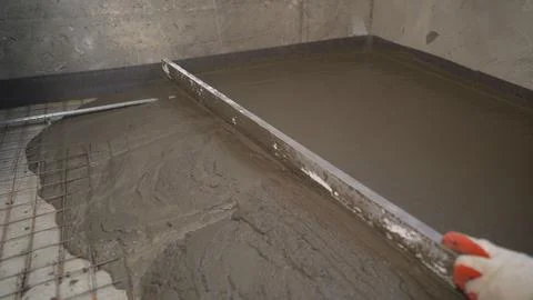 A builder in protective gloves pours a self-levelling screed onto the floor a Stock Photos