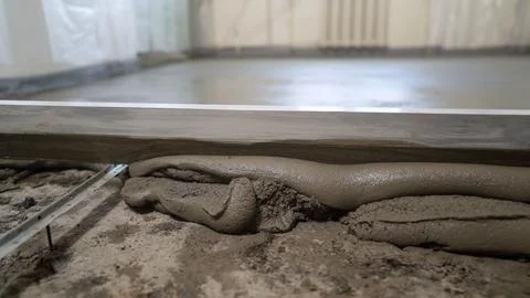 A builder in protective gloves pours a self-levelling screed onto the floor a Stock Photos