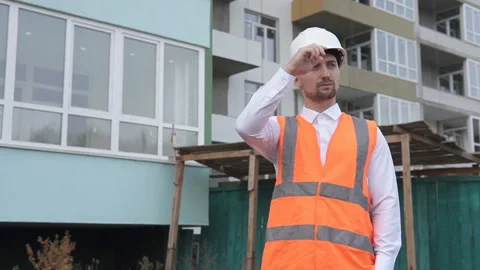 The builder puts on a white helmet and looks at a high-rise monolithic building Video stock 118968736