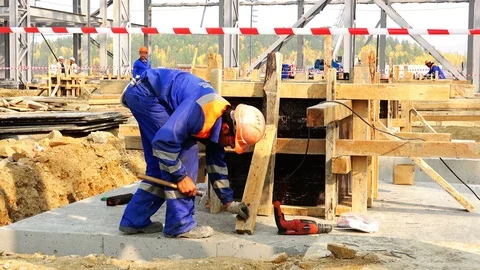 The builder in a robe and helmet secures the support for the foundation formwork Stock Footage 74004208