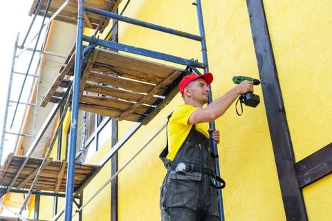 Builder with screwdriver attaches facade timber, decorative half-timbered s.. 스톡 사진