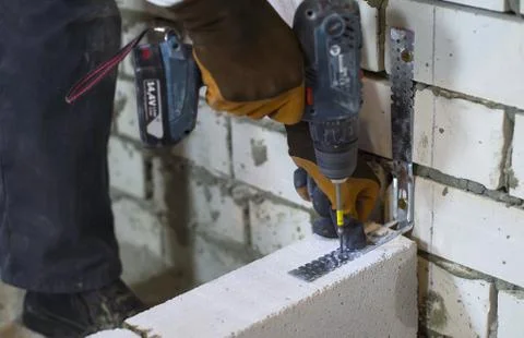 Builder screwing joining clamp in aerated concrete block with electric drill Stock Photos