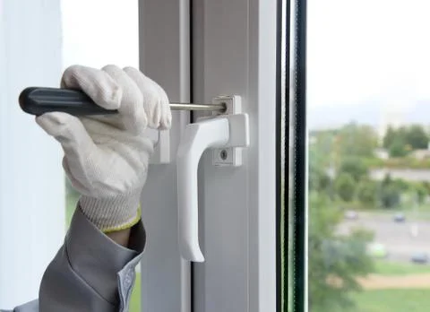 The builder screws the handle of the window frame with a screwdriver. Stock Photos