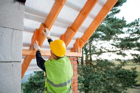 Builder secures roof joist using tool, house under construction with visibl.. Stock Photos