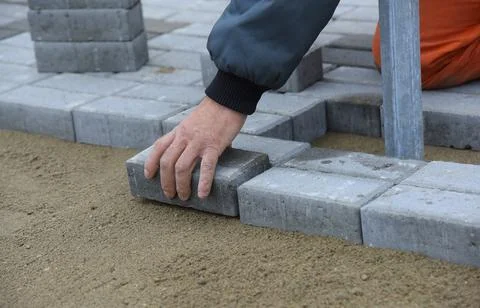 The builder settles the paving slabs in even rows. Stock Photos