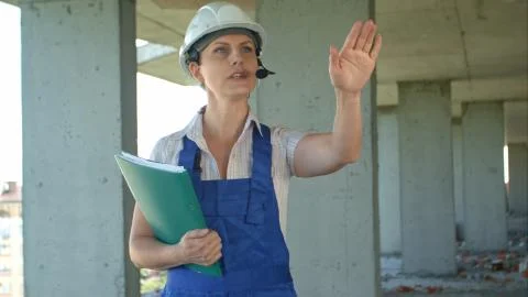 Builder supervisor oversees building site and gives instructions to workers over Stock Photos