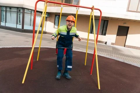 Builder is swinging on swing at the playground of the future multi-story buil Stock Photos