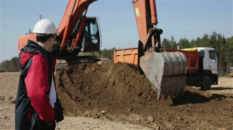 A builder talking on the phone, an excavator working Stock Footage 62703224